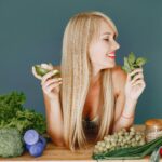 mulher jovem em sua cozinha, segurando uma tigela colorida de comida saudável com expressão leve, representando alimentação saudável e conveniente