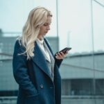 mulher refletindo com o celular na mão em um ambiente claro, representando sobrecarga de informação e busca por clareza